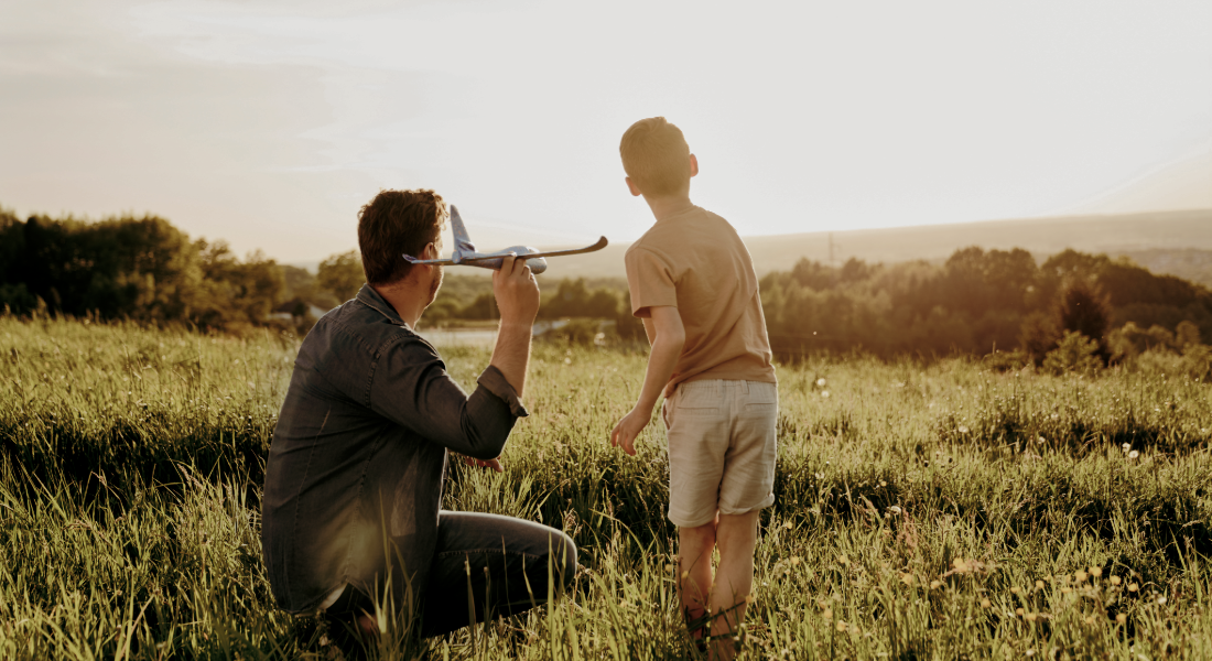 young boy and his father in a field playing with a toy plane